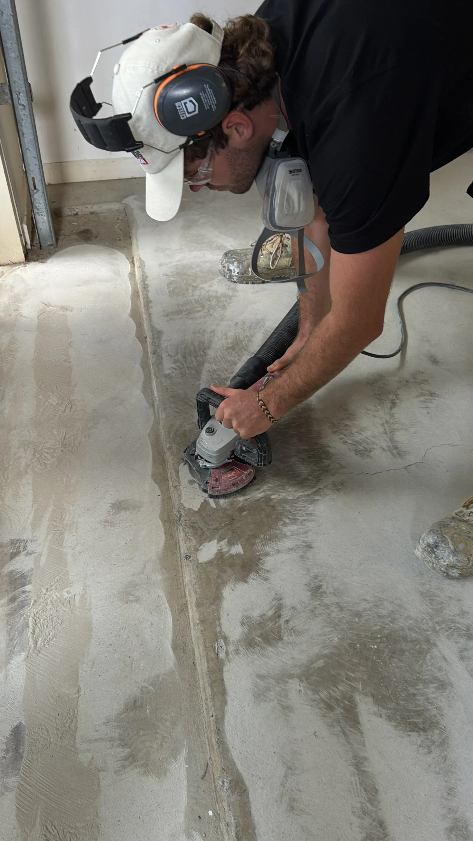 Worker diamond-grinding concrete floor in preparation for epoxy coating, showing dramatic before-and-after